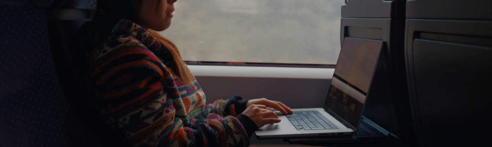 Traveller using a laptop on a train, representing embedded travel insurance offered during booking